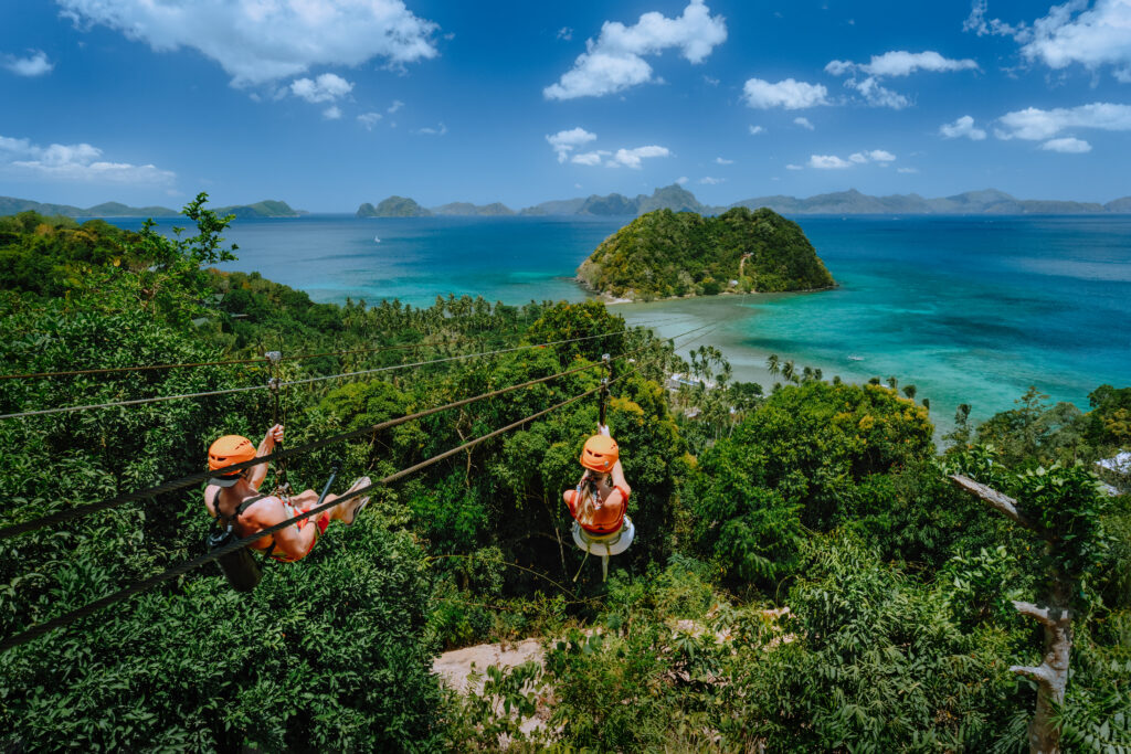 Zipline over Las Cabanas Beach with tourist on sunny day with white clouds over sea. El Nido, Palawan, Philippines.